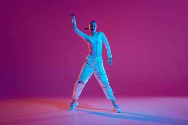 Beyaz kıyafetli, yetenekli ve sanatsal genç kız neon ışıkta pembe arka planda hip-hop dansı yapıyor. Serbest stil dansı, modernlik, şehir kültürü, gençlik kavramı