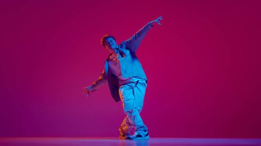 Genç sanatsal ve yetenekli adam için dinamik bir imaj. Günlük giysiler içinde hip-hop yapıyor. Pembe arka planda neon ışıkta antrenman yapıyor. Serbest stil dansı, modernlik, şehir kültürü, gençlik kavramı