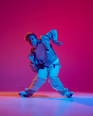 Dans kulübü üyesi. Hareketli gündelik giysiler içindeki genç enerjik adam, neon ışıkta pembe arka planda hip hop dansı yapıyor. Serbest stil dansı, modernlik, şehir kültürü, gençlik kavramı