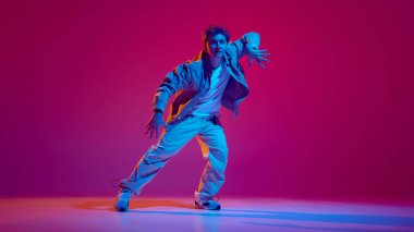Sıradan kıyafetler içinde etkileyici ve yetenekli genç adam, neon ışıkta pembe arka planda hip-hop dansı yapıyor. Serbest stil dansı, modernlik, şehir kültürü, gençlik kavramı