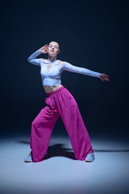 Şık giyinmiş, sahnede hip-hop yapan, lacivert arka planda dans eden güzel bir genç kızın tam boy görüntüsü. Serbest stil dansı, modernlik, şehir kültürü, gençlik kavramı
