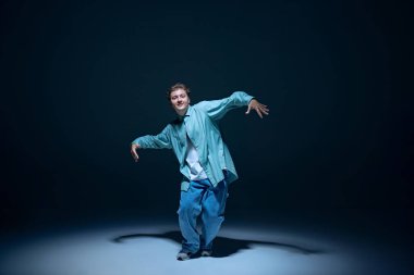 Hareket halindeki günlük giysiler içindeki genç adam için dinamik bir görüntü, lacivert arka planda hip-hop dansı. Gölgeler. Serbest stil dansı, modernlik, şehir kültürü, gençlik kavramı