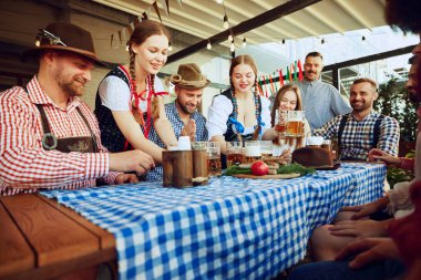 İki kadın, Bavyera kıyafeti giymiş garson bir grup arkadaşa bira servisi yapıyor. Barda neşeli bir kutlama için toplanıyorlar. Ekim Festivali, festival, parti, bira fabrikası, gelenek kavramı