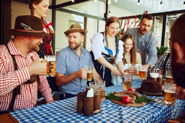 Oktoberfest neşesi. Erkekler ve kadınlar, yerel bardaki masada oturan arkadaşlar, biranın tadını çıkarıyorlar. Bavyera gelenekleriyle kutlama. Ekim Festivali, festival, parti, bira fabrikası, gelenek kavramı