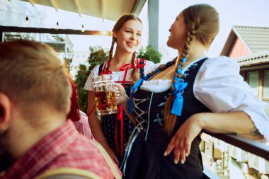 Geleneksel Bavyera kıyafetleri içinde iki güzel genç bayan, barda durmuş neşeyle konuşuyorlar. Ekim Festivali, festival, parti, bira fabrikası, gelenek kavramı