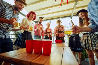 Dostlar, Ekim Festivali 'nde canlı bir bira pongu için toplanıyor. Kahkaha, rekabet ve bira kupaları havayı kutlamakla dolduruyor. Ekim Festivali, festival, parti, bira fabrikası, gelenek kavramı