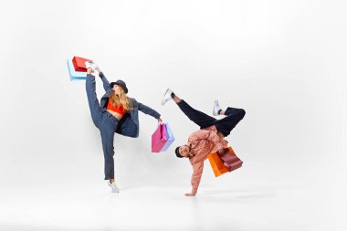 Şık ve enerjik genç insanlar, break dans pozisyonunda erkek ve yüksek tekme atan kadın, her ikisi de renkli alışveriş torbaları tutuyor. Alışveriş, satış, Kara Cuma, moda, tatil kavramı