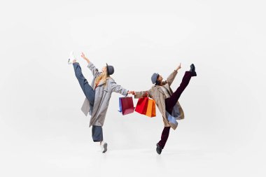 Renkli alışveriş torbalarıyla ayakta duran, başarılı alışveriş ve iyi satışları kutlayan dinamik ve şık iki genç kadın. Alışveriş, satış, Kara Cuma, moda, tatil kavramı