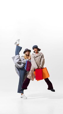 Eğlence ve zarafeti dengeleyen, alışveriş çantalı iki kadın, beyaz arka planda izole edilmiş, satış maceralarına eğlenceli bir hava katıyor. Alışverişkolik. Alışveriş, satış, Kara Cuma, moda, tatil kavramı
