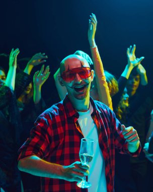 Komik palyaço makyajıyla neşeli bir şekilde dans edip içmeye odaklan. Cadılar Bayramı kutlaması için gece kulübünde toplanan arkadaşlar. Cadılar Bayramı kavramı, tatil, parti, eğlence