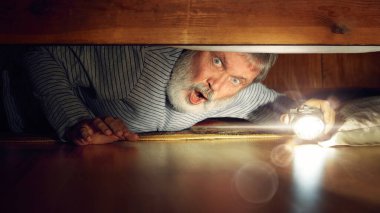 Yatağın altına el feneriyle bakan duygusal son sınıf öğrencisi, şok duygularını ifade ediyor. Evde korkunç bir gece. Cadılar Bayramı kavramı, insan duyguları, ürkütücü sezon.