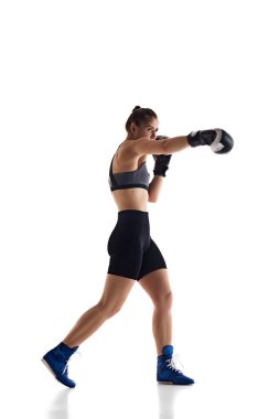 Sportif vücutlu, boks baskılı, yumruk atma tekniği olan, beyaz stüdyo arka planında izole genç bir kızın tam boy görüntüsü. Spor anlayışı, hobi, aktif ve sağlıklı yaşam tarzı
