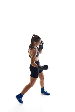 Formda vücutlu, sportif bir genç kadın, hareketli bir boks sporcusu, beyaz stüdyo arka planında izole edilmiş yumruklar deniyor. Spor anlayışı, hobi, aktif ve sağlıklı yaşam tarzı