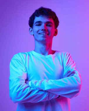 Gülümseyen genç bir adamın portresi, beyaz uzun kollu gömlek giyen bir öğrenci, neon ışıklarıyla değişen pembe stüdyo resmine karşı. İnsan duyguları, gençlik, yaşam tarzı, moda kavramı