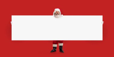 Noel Baba boş pankartın üzerinden bakıyor, bayram mesajını paylaşmaya hazır, neşeli ruhu tuhaf, cüce benzeri cazibeyle harmanlıyor. Noel, yeni yıl, 2024. Poster, kartpostal, broşür