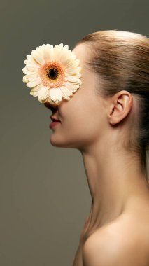 Pürüzsüz, lekesiz, yeşil arka planda Gerbera çiçeğiyle poz veren güzel genç bir kadının yan görüntüsü. Doğal kadın güzelliği, cilt bakımı, kozmetik ve kozmetik kavramı