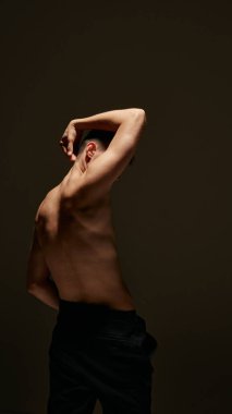 Pantolonsuz poz veren genç adamın arka görüntüsü, mükemmel, sportif vücudunu gösteriyor, karanlık stüdyo geçmişine karşı güçlü bir rahatlama. Erkek güzelliği, vücut ve cilt bakımı, sağlık ve spor kavramı