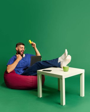 Çevrimiçi alışveriş aktivitesi. Kolay ve uygun alışverişler. Genç sakallı adam yeşil stüdyo geçmişine karşı dizüstü bilgisayarla emir veriyor. Alışveriş, satış, Kara Cuma, Siber Pazartesi