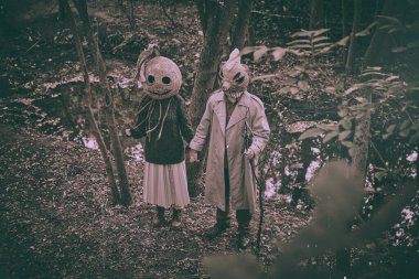 Ormanın derinliklerinde ürkütücü maskeler takmış, garip kıyafetler giymiş, el ele tutuşmuş korkunç insanlar. Eski tarz fotoğrafçılık. Cadılar Bayramı kavramı, ürkütücü sezon, eski tarz..