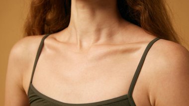 Kırpılmış kadın bedeni, köprücük kemiği. Üstte manken pozu veriyor, sağlıklı ve ince vücudunu kumlu renkli stüdyo arka planına karşı gösteriyor. Doğal kadın güzelliği, vücut ve cilt bakımı, sağlık kavramı