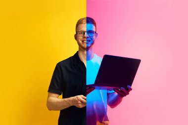 Gözlüklü genç adam, öğrenci, çalışan, dizüstü bilgisayarı sarı ve pembe neonlu tutan serbest çalışan. Üretkenlik, dijitalleşme, çevrimdışı ve çevrimiçi işler. İnsan duyguları kavramı, çeşitlilik