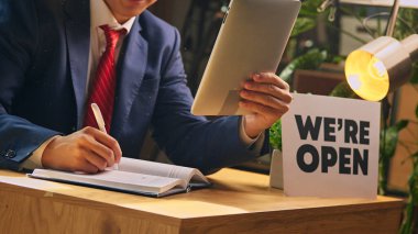 Resmi görevdeki işadamı masada otururken tableti tutarken ve not alırken açık tabela kullanıyoruz. Kesilmiş görüntü. Yeni iş, başlangıç, başarı, ilerleme kavramı