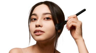 Güzel, lekesiz ciltli genç bir Koreli kızın portresi. Çıplak makyajını yapıyor, kızarmak için fırça kullanıyor. Doğal güzellik kavramı, cilt bakımı, kozmetik ve kozmetik.