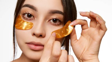 Koreli kadın göz altı bantları uyguluyor, şişkinliği azaltmak ve doğal güzellik, cilt bakımı, kozmetik ve kozmetik kavramını parlatmak için cilt rutinini vurguluyor.