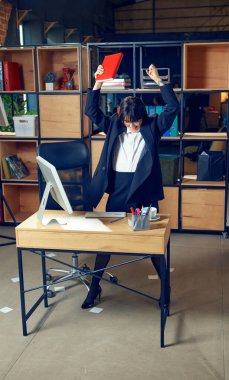 Resmi olarak duygusal genç bir kadın ofiste ayakta durup saf heyecanı ifade ederek işindeki zaferi sembolize eder. İş kavramı, başarı, başarı, mutluluk