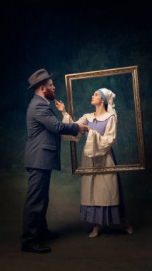 Eski moda kıyafetler giyen bir çift romantik bir anı paylaşıyor, resim çerçevesinde el ele tutuşuyorlar, sanat ve hayatı eşsiz bir portrede harmanlıyorlar. Sanat kavramı, dönem karşılaştırması, yaratıcı vizyon, reklam