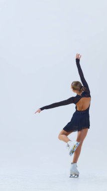 Zarif ve yetenekli genç kız, siyah sahne kostümlü artistik patinajcı, beyaz arka planda tek başına dans ediyor. Profesyonel spor anlayışı, performans. Boşluğu kopyala, ad