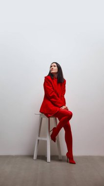 Kırmızılı kadın tabureye oturmuş, sakin ve düşünceli bir ifadeyle yukarıya bakıyor. Psikoloji kavramı. Kendine güven, güven, gurur ve başarı. İyimserlik ve içsel güç.