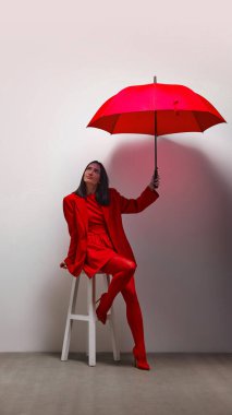 Kırmızılı kadın elinde eşleşen şemsiyeyle, sıcaklık ve korunma sahnesi yaratıyor. Şemsiye barınağı ve duygusal güvenliği sembolize eder. Psikoloji, renk, duygu, özgüven ve güvenlik kavramı
