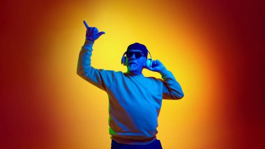 Güneş gözlüklü yaşlı adam kulaklıkla müzik dinliyor sarı stüdyo ışıklarıyla. İnsan duyguları kavramı, yaşlı yaşam tarzı. Boşluğu kopyala, ad