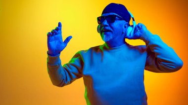 Güneş gözlüklü yaşlı adam kulaklıkla müzik dinliyor sarı stüdyo ışıklarıyla. İnsan duyguları kavramı, yaşlı yaşam tarzı. Boşluğu kopyala, ad