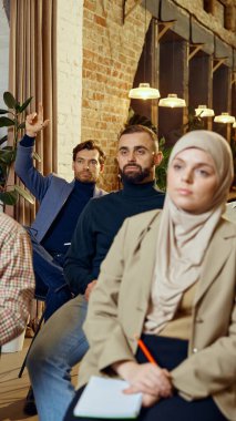 Genç adam atölye çalışması sırasında dikkatlice el kaldırıyor, nişan işareti veriyor. Seminere katılan bir grup çok kültürlü insan. İş dünyasında dei kavramı, takım çalışması, işbirliği, öğrenme