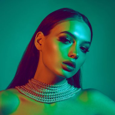 Çift tonlu yeşil ve mavi ışık altında genç güzel bir kadının yakın plan portresi kusursuz cildini, çarpıcı özelliklerini ve modaya uygun makyajını vurguluyor. Kadın güzelliği kavramı, yüksek moda.