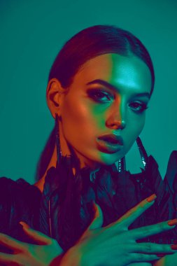 Moda makyajlı, şık küpeli, parlak arkaplanda tüylerle poz veren güzel bir kadının göz kamaştırıcı portresi. Kadın güzelliği kavramı, yüksek moda.