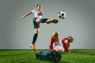 İki genç kadının dinamik görüntüsü, sahada yarışan futbolcular, kazanmak için beceri ve motivasyon gösteriyorlar. Beyaz formalı kadın havada topa vuruyor. Spor, eylem, rekabet, oyun kavramı