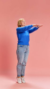 Sağlık durumunu kontrol ediyorum. Normal giyinmiş olgun, yaşlı bir kadın. Pembe stüdyo arka planında vücut dengesini gösteriyor. Kıdemli yaşam tarzı kavramı, duygular, sağlık, bakım, sağlık