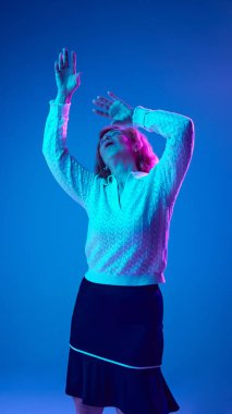 Olumlu, yaşlı bir kadın neon ışıkta mavi stüdyo arka planında neşeyle dans ediyor. Kıdemli yaşam tarzı kavramı, duygular, sağlık, bakım, sağlık