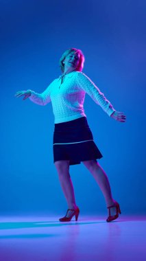 Olumlu, yaşlı bir kadın neon ışıkta mavi stüdyo arka planında neşeyle dans ediyor. Kıdemli yaşam tarzı kavramı, duygular, sağlık, bakım, sağlık