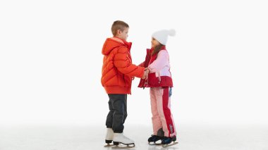 Destek. Mutlu küçük kız ve erkek kardeş, şık, sıcak giysiler içinde erkek ve kız buz pateni pistinde el ele tutuşup birlikte oturuyorlar. Kış kavramı, tatil, tatil, boş zaman aktivitesi