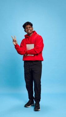 Tam boy. İnternette haberleşmek için tablet kullanan sıradan giysili genç Hintli adam, mavi stüdyo geçmişine karşı komik mim yüzüyle ayakta duruyor. Duyguların kavramı, yaşam tarzı, eğitim