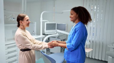 Mavi önlüklü diş hekimi, dişçi muayenehanesinde dostane ve misafirperver bir ortam yaratarak yaşlı hastayı sıcak bir şekilde selamlıyor. Sağlık sigortası, güzellik, hijyen, dişçi danışmanlığı kavramı. Ad.