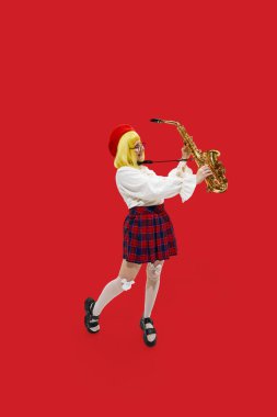 Mutlu, heyecanlı, şık giyinmiş, sarı peruklu, saksafonlu, parlak kırmızı arka planlı, şık bir kadın. İş anlayışı, meslek anlayışı, insan duyguları ve yüz ifadeleri. Ad