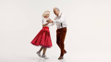 Elderly couple, woman in polka dot skirt and man with suspenders, enjoying swing dancing isolated on white background. Concept of retro dance, hobby, aging, active lifestyle. Happiness and joy clipart