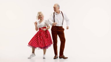 Elderly couple dancing together with smiles and enthusiasm isolated on white background. Woman wearing polka dot skirt, and man in suspenders. Concept of retro dance, hobby, aging, active lifestyle clipart