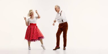 Yaşlı adam ve kadın, beyaz arka planda izole edilmiş retro-esinlenmiş kıyafetlerle neşeli dans ediyorlar. Klasik swing dansının zarafeti. Retro dans, hobi, yaşlanma, aktif yaşam tarzı kavramı