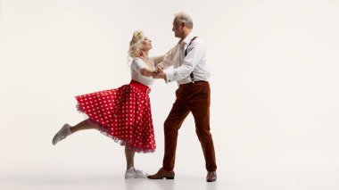 Cheerful elderly couple dancing together, woman in red polka dot skirt and man in suspenders isolated on white background. Concept of retro dance, hobby, aging, active lifestyle clipart